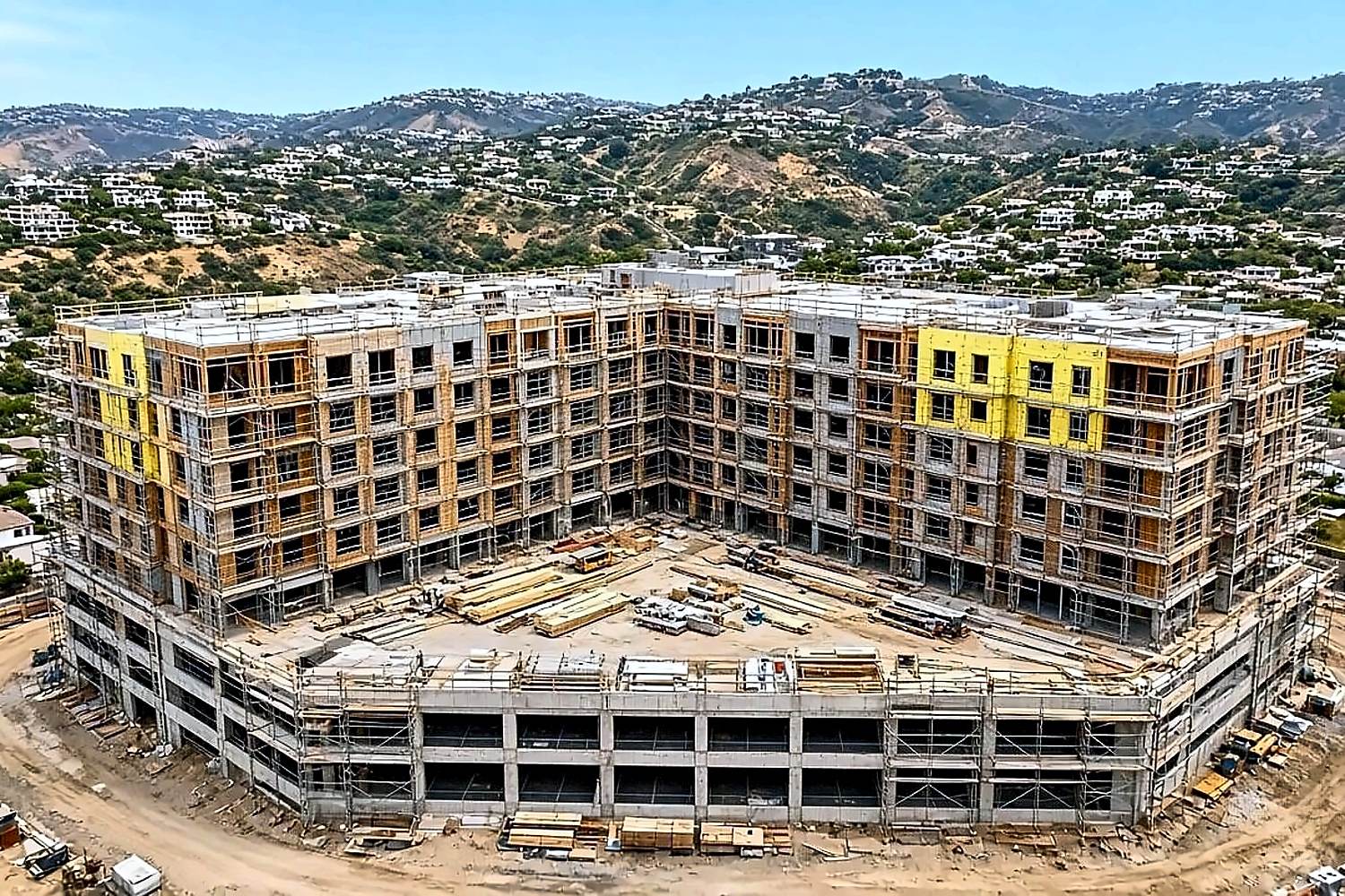 Aerial of large L-shaped mid-rise multifamily framing on hillside